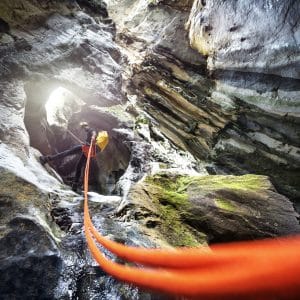 Low angle view of a member of canyoning team with yellow helmet and backpack moving down the cliff in the canyon.