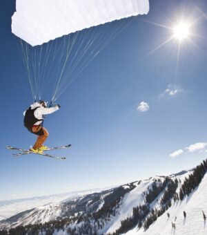 Extreme sports. Action shot of a speed flyer zooming past, high above a mountain peak towards the sun.