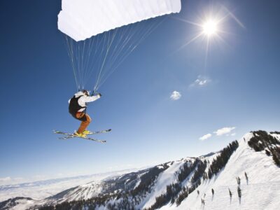 Extreme sports. Action shot of a speed flyer zooming past, high above a mountain peak towards the sun.