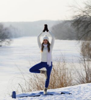 Yoga Smiling young woman standing on one leg in asana, near winter river