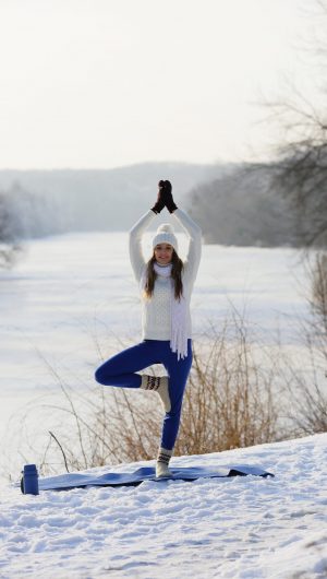 Yoga Smiling young woman standing on one leg in asana, near winter river