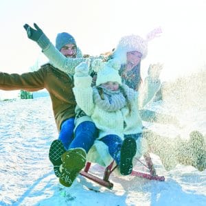 Familie fährt begeistert auf dem Schlitten durch den Schnee im Winter